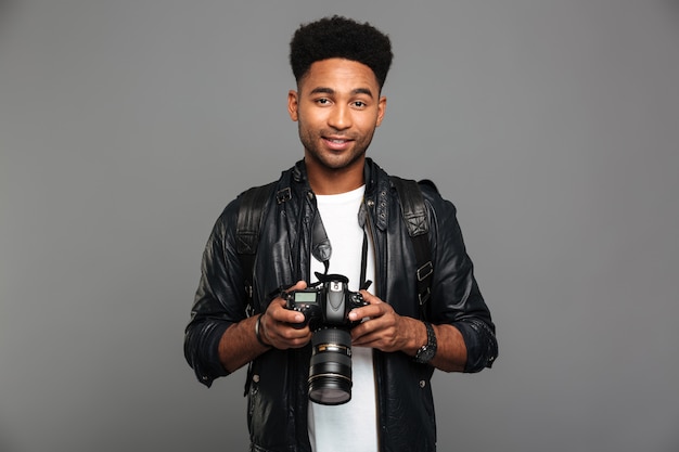 Giovane uomo afroamericano sorridente attraente che tiene macchina fotografica digitale, guardante