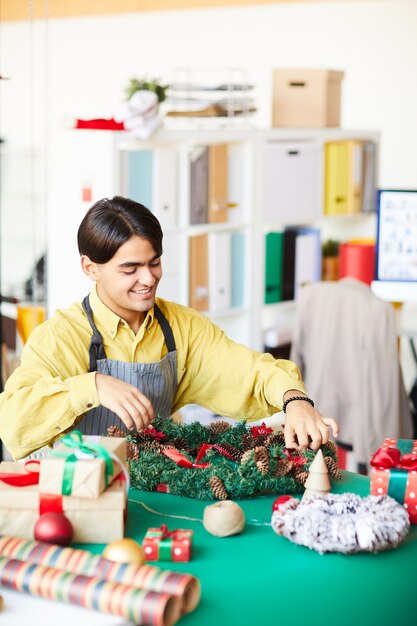 Giovane uomo al lavoro, facendo una ghirlanda di Natale e confezionando regali