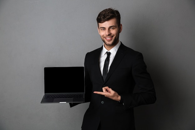 Giovane uomo allegro di affari che mostra esposizione del computer portatile