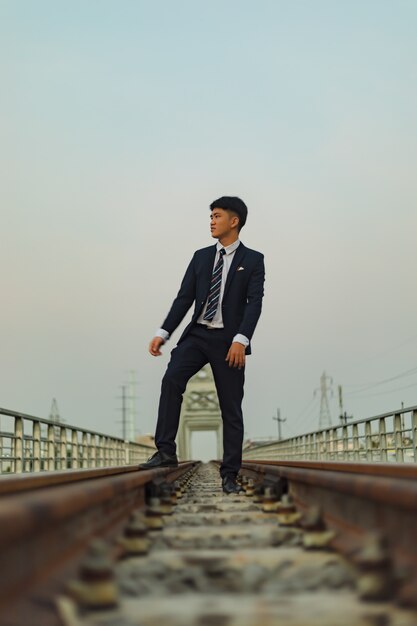 Giovane uomo asiatico in un vestito staning nel mezzo di una ferrovia mentre guarda lontano