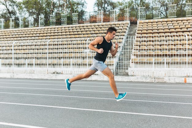 Giovane uomo atletico che corre sullo stadio al mattino