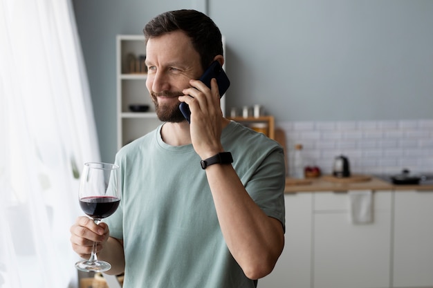 Giovane uomo barbuto che beve vino e parla al telefono