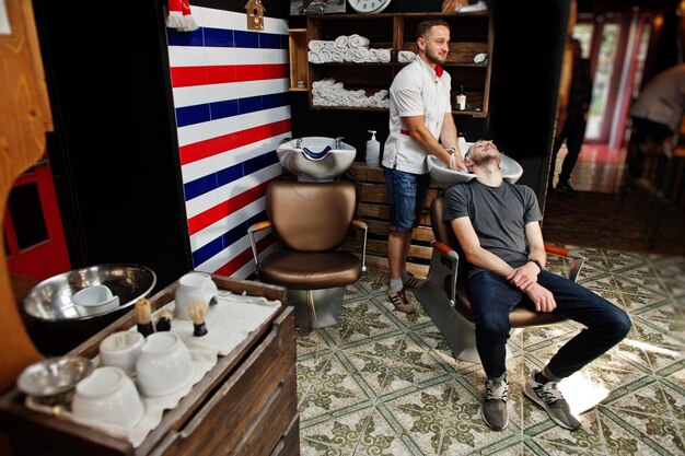 Giovane uomo barbuto che lava la testa dal parrucchiere mentre è seduto su una sedia al barbiere Barber soul