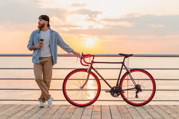 Giovane uomo barbuto che viaggia in bicicletta al tramonto sul mare