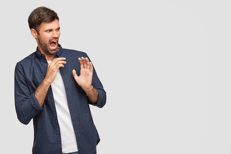 Foto gratuito giovane uomo barbuto disperato e irritato con espressione facciale negativa, dice fie, spinge le mani, vede qualcosa di disgustoso e spiacevole, sta contro un muro bianco con copia spazio sulla destra