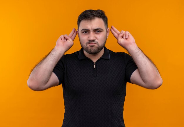 Giovane uomo barbuto in camicia nera che guarda l'obbiettivo con la faccia arrabbiata gesticolando con le mani