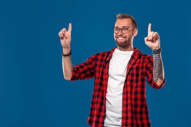 Giovane uomo barbuto sorridente in una camicia a scacchi che mostra la direzione con il dito. Isolato su sfondo blu. Fricchettone