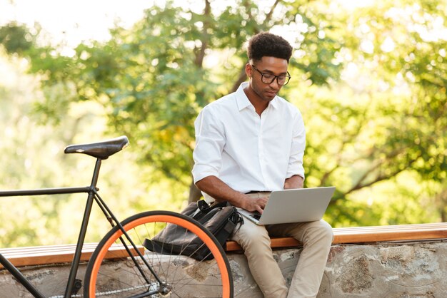 Giovane uomo bello africano che per mezzo del computer portatile.