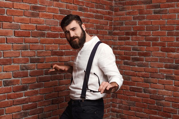 Giovane uomo bello che balla in posa sul muro di mattoni.