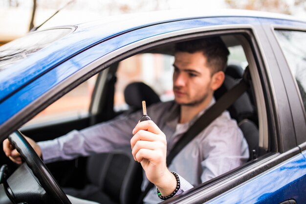 Giovane uomo bello che guida la sua nuova auto, tendendo le chiavi