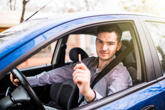 Giovane uomo bello che guida la sua nuova auto, tendendo le chiavi