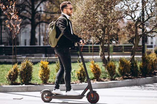 Giovane uomo bello che guida su scooter nel parco