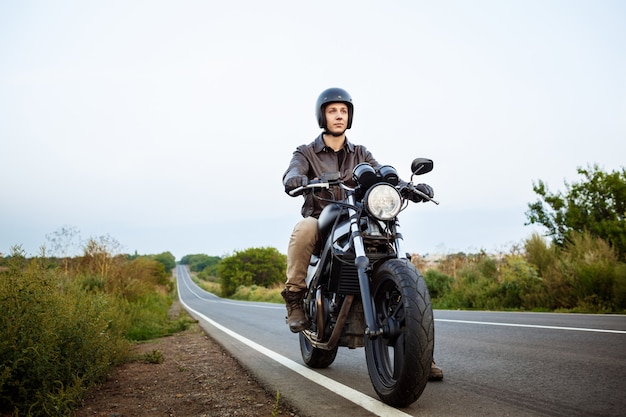 Giovane uomo bello che guida su una moto a strada di campagna.