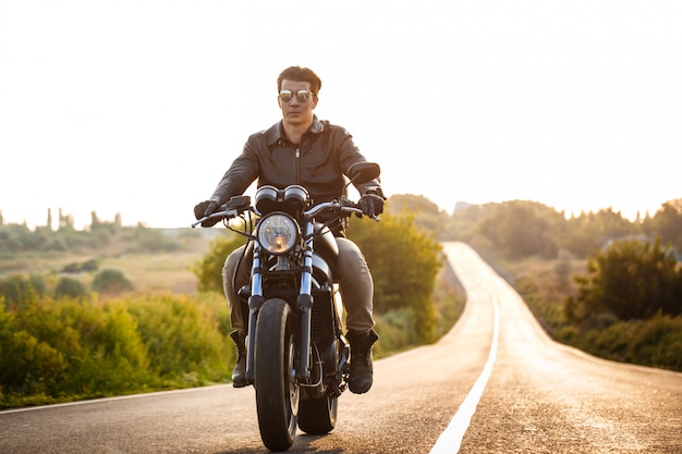 Giovane uomo bello che guida su una moto a strada di campagna.