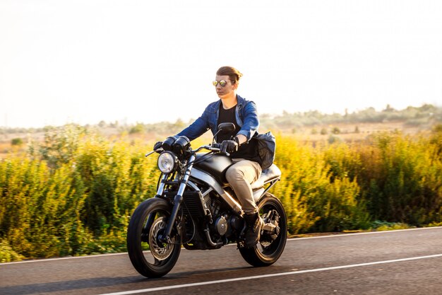 Giovane uomo bello che guida su una moto a strada di campagna.