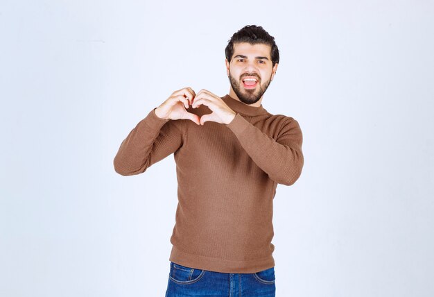 Giovane uomo bello che indossa abiti casual sorridendo e facendo la forma del simbolo del cuore con le mani. Foto di alta qualità