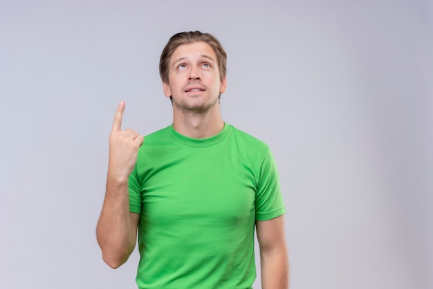 Giovane uomo bello che indossa la maglietta verde che indica il dito verso l'alto