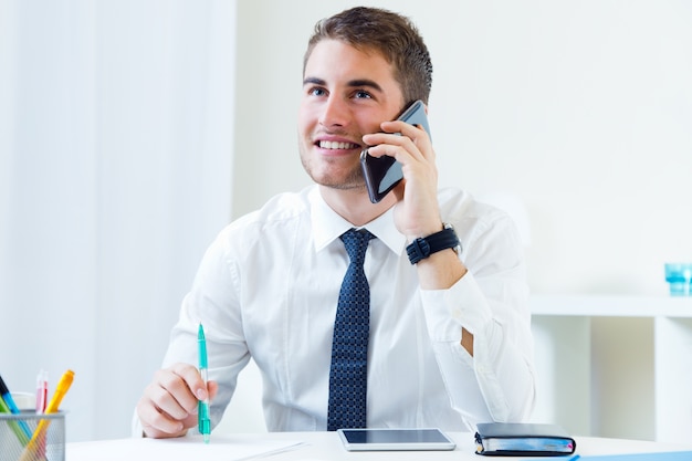 Giovane uomo bello che lavora nel suo ufficio con il telefono cellulare.