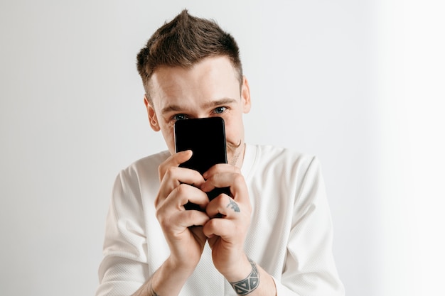 Giovane uomo bello che mostra lo schermo dello smartphone isolato su grigio walll in stato di shock con una faccia a sorpresa