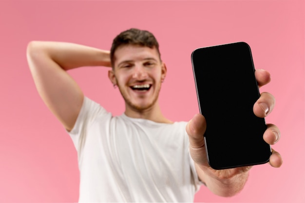 Giovane uomo bello che mostra lo schermo dello smartphone isolato su sfondo rosa in stato di shock con una sorpresa