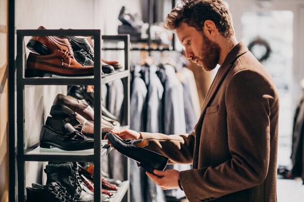 Giovane uomo bello che sceglie le scarpe ad un negozio