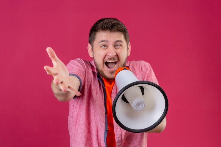 Foto gratuito giovane uomo bello che tiene il megafono che gli grida in piedi con la mano alzata