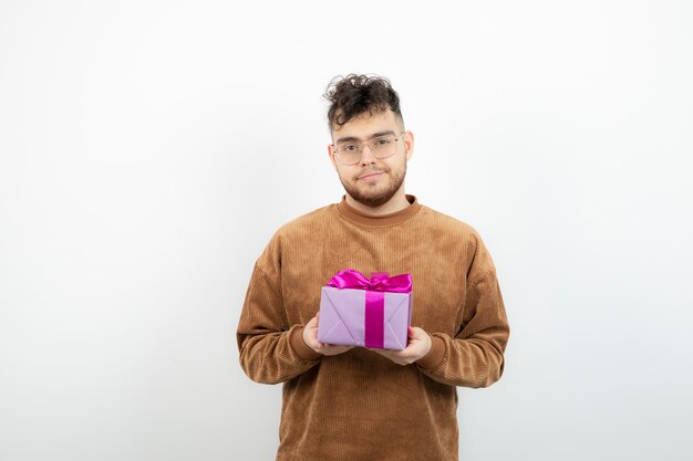 Giovane uomo bello che tiene il suo regalo di compleanno sopra bianco.