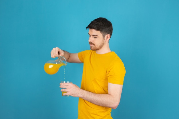 Giovane uomo bello che versa il succo al bicchiere su un blu.