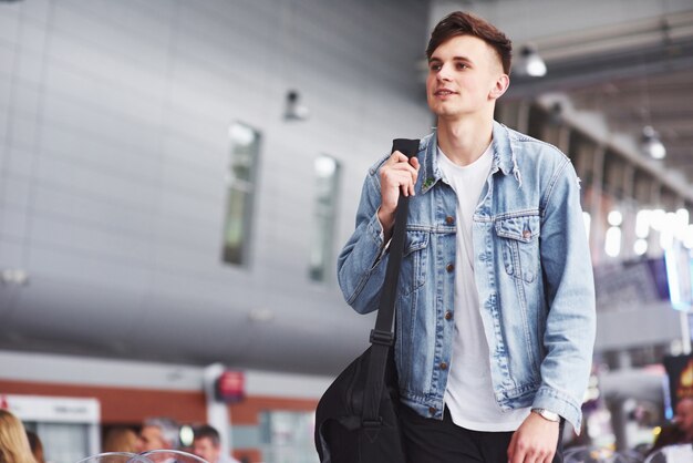 Giovane uomo bello con una borsa sulla spalla in fretta per l'aeroporto.