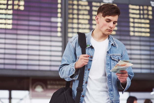 Giovane uomo bello con una borsa sulla spalla in fretta per l'aeroporto.