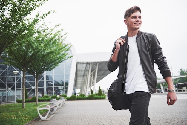 Giovane uomo bello con una borsa sulla spalla in fretta per l'aeroporto.