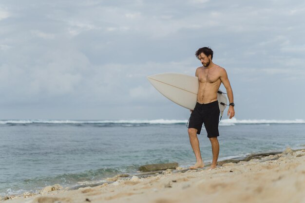 Giovane uomo bello con una tavola da surf sull'oceano.