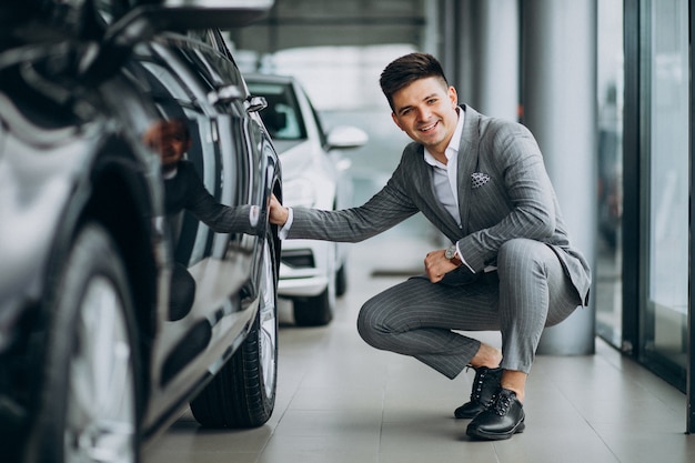 Giovane uomo bello di affari che sceglie un'automobile in una sala d'esposizione dell'automobile