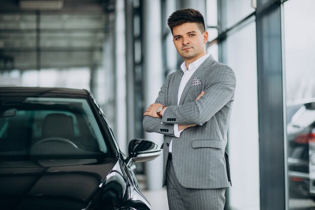 Giovane uomo bello di affari che sceglie un'automobile in una sala d'esposizione dell'automobile