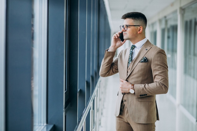 Giovane uomo bello di affari che sta con il telefono all'ufficio