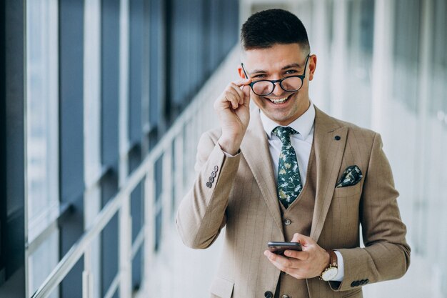 Giovane uomo bello di affari che sta con il telefono all'ufficio