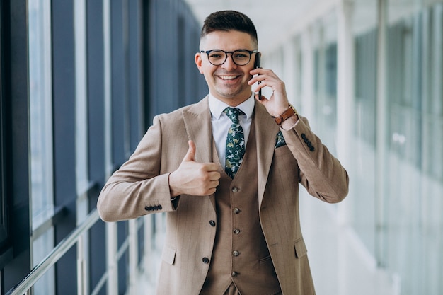 Giovane uomo bello di affari che sta con il telefono all'ufficio