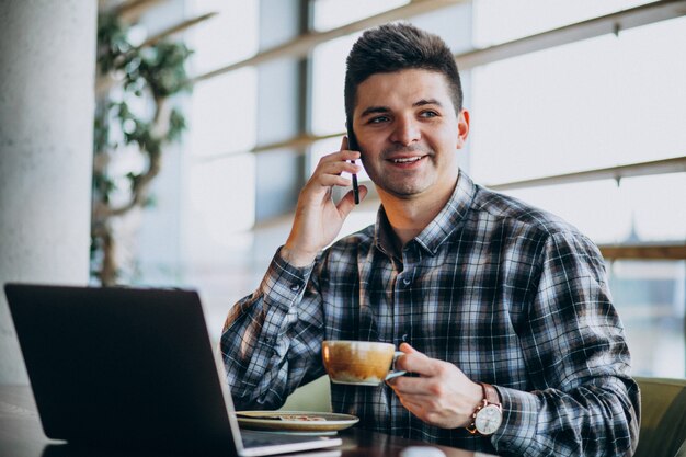 Giovane uomo bello di affari che utilizza computer portatile in un caffè