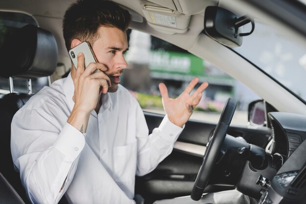 Giovane uomo bello in auto parlando sul telefono cellulare che gesturing