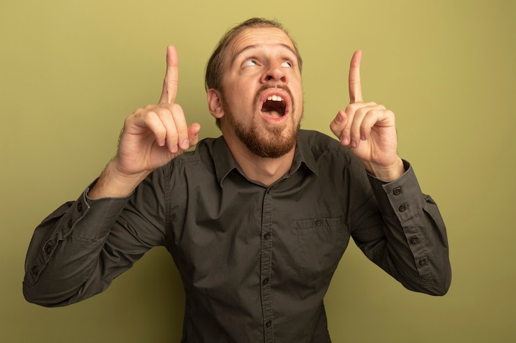 Foto gratuito giovane uomo bello in camicia grigia che osserva in su sorpreso e stupito mostrando le dita indice
