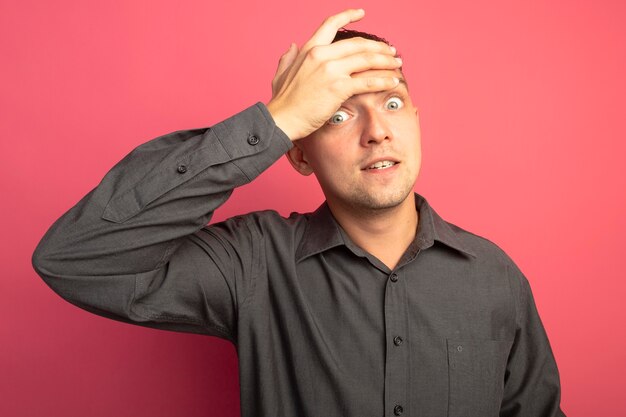 Giovane uomo bello in camicia grigia che sembra preoccupato e confuso con la mano sulla fronte