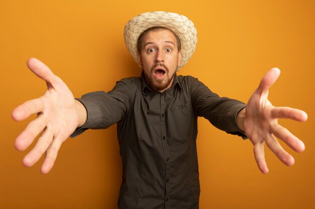 Giovane uomo bello in camicia grigia e cappello estivo preoccupato con le braccia fuori