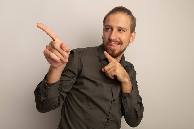 Giovane uomo bello in camicia grigia felice e positivo che punta con il dito indice a lato