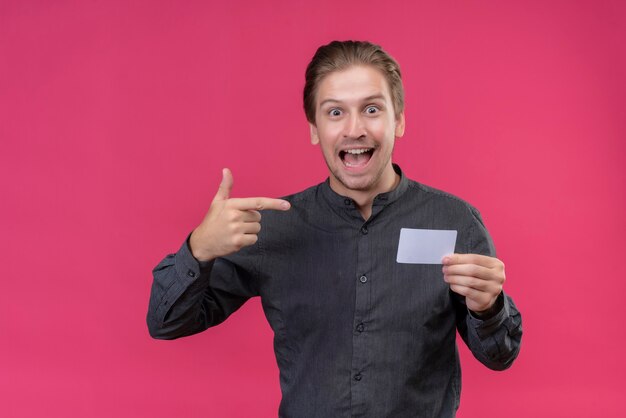 Giovane uomo bello in camicia nera che tiene il telefono cellulare che punta con il dito ad esso