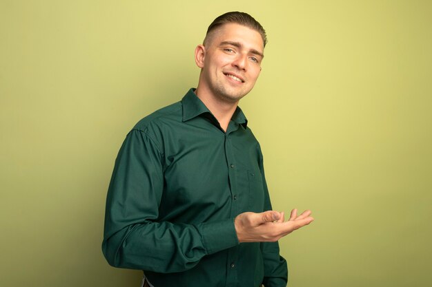 Giovane uomo bello in camicia verde che presenta qualcosa con il braccio della sua mano che sorride