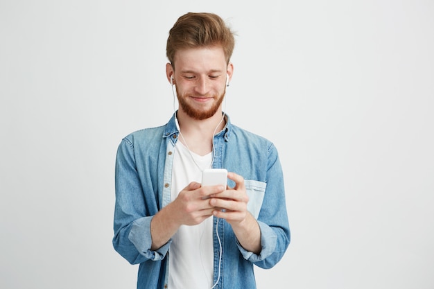 Giovane uomo bello in cuffie che sorride esaminando telefono che ascolta la musica in streaming.