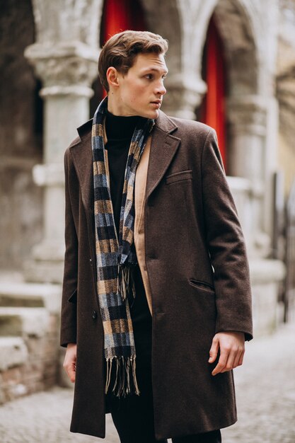 Giovane uomo bello in un cappotto fuori strada