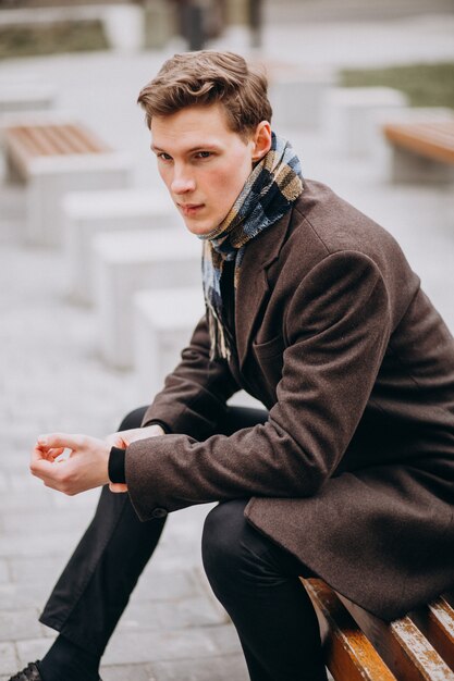 Giovane uomo bello in un cappotto fuori strada