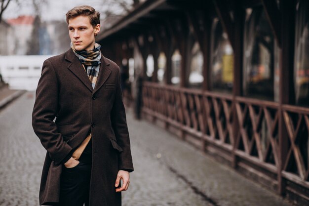 Giovane uomo bello in un cappotto fuori strada