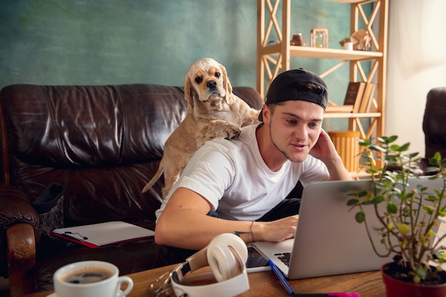 Giovane uomo bello seduto sul divano marrone e lavora con il suo simpatico cane